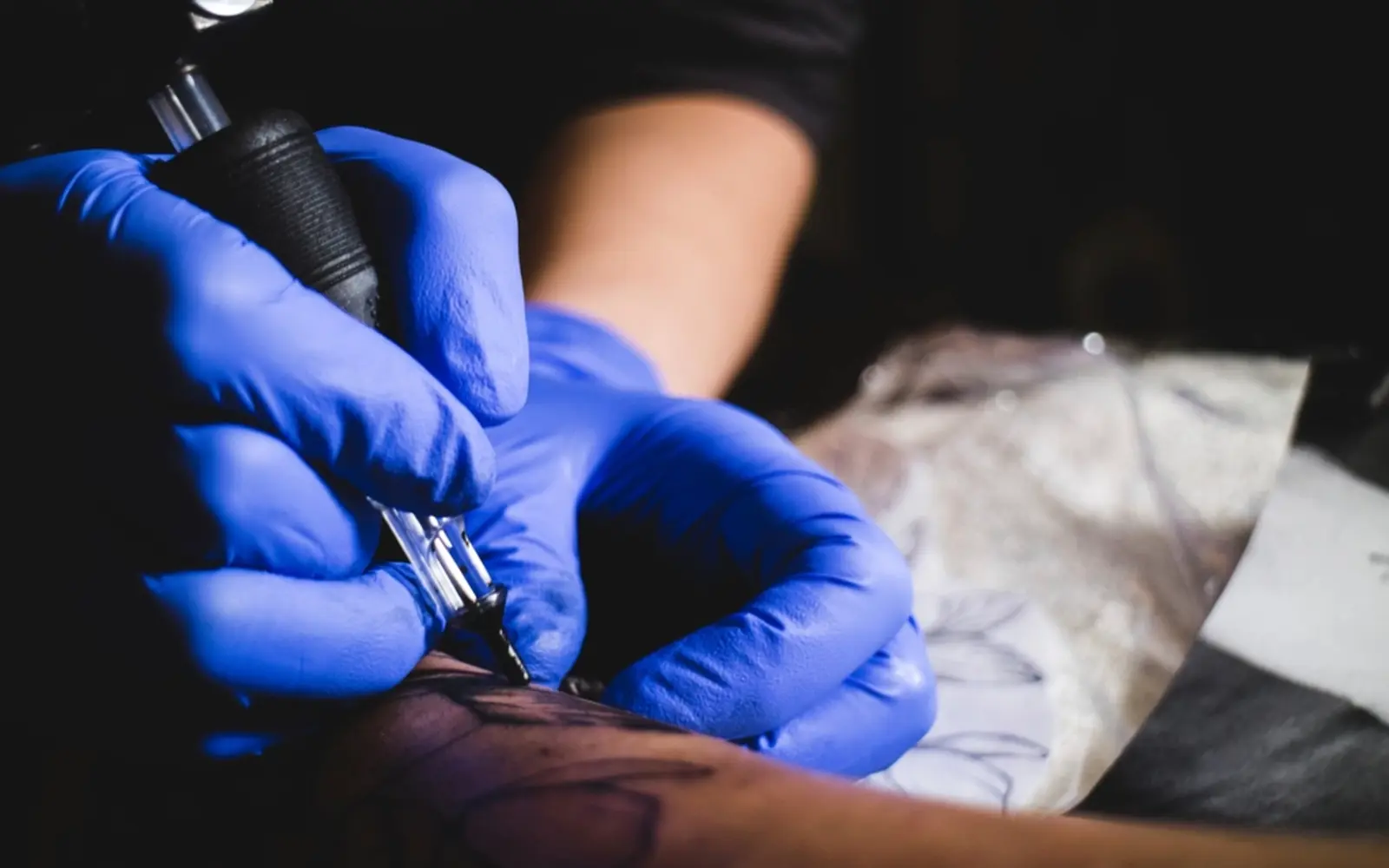 A tattoo artist at work wearing blue gloves